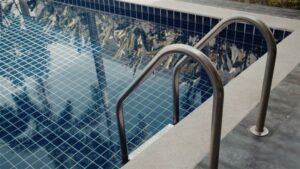 The pool coping here is a flat, Light-Gray stone or concrete slab that overhangs the interior blue tiles.