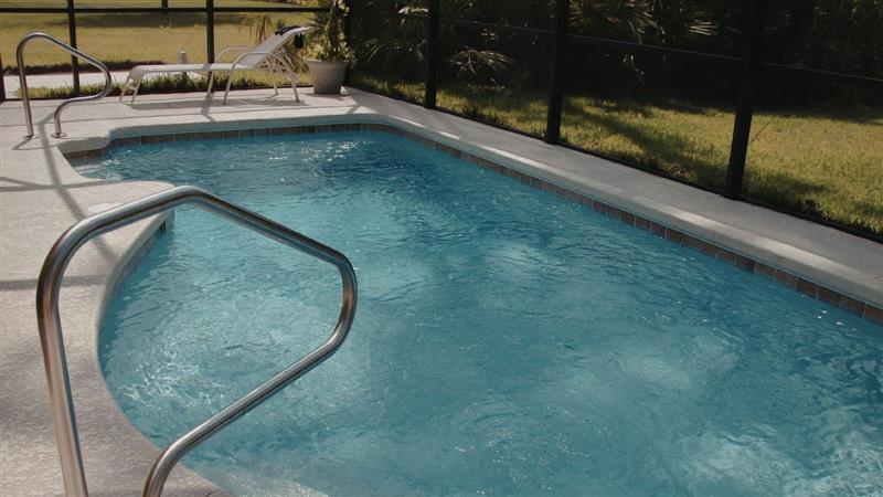 A bright, clear blue swimming pool inside a screened-in enclosure, featuring a light-colored, textured concrete deck